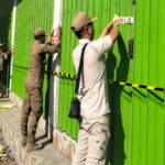 Petugas Satpol PP Sampang ketika memasang sticker bertuliskan segel pada bangunan ruko yang berdiri didepan puri matahari Kelurahan Karang Dalam, Sampang.